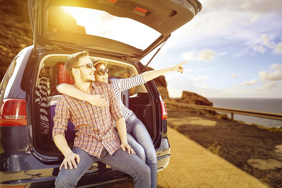 Personal Insurance - Young Couple Sitting in the Back of Their Car and Pointing During a Summer Car Trip at Sunset